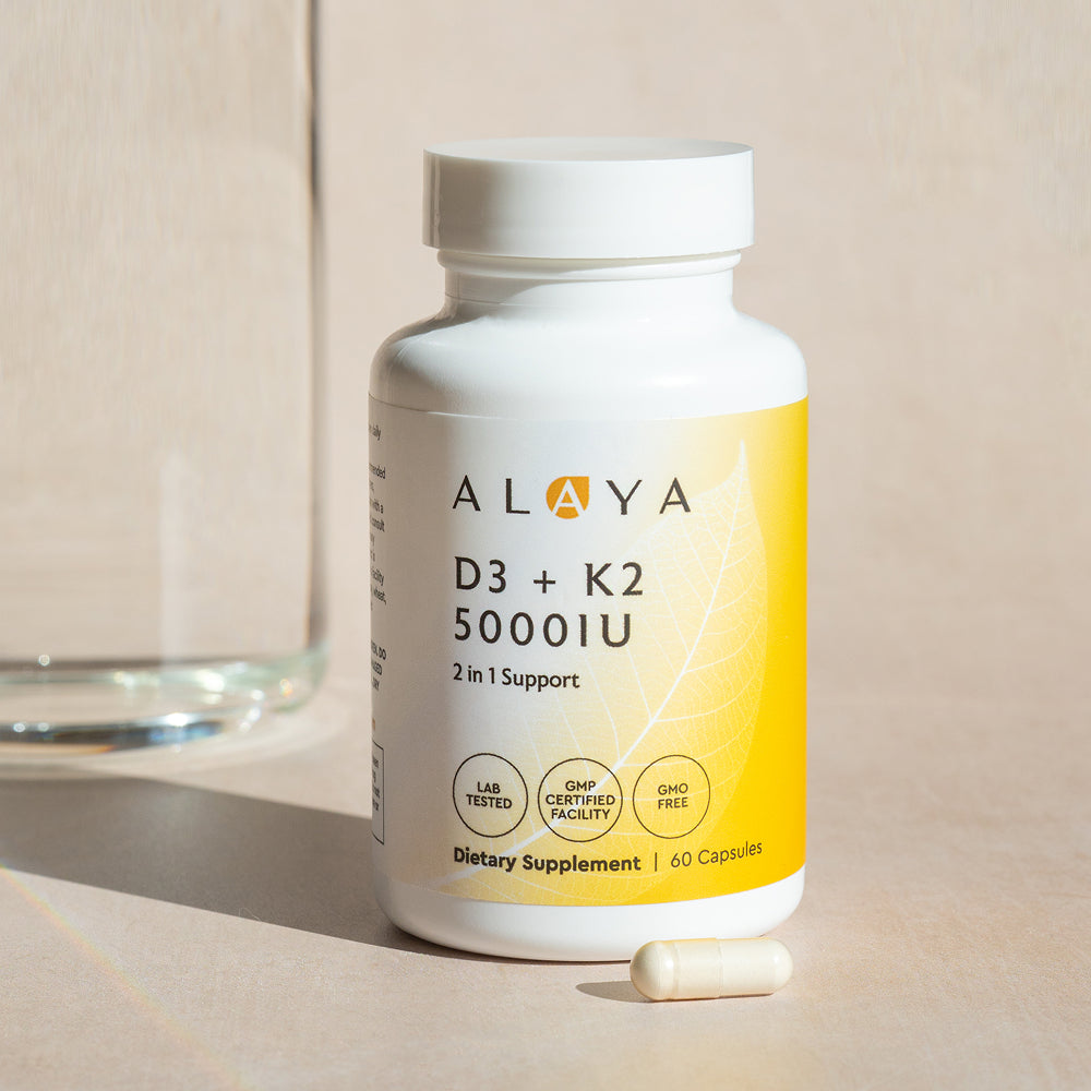 Alaya D3 + K2 dietary supplement bottle on a beige surface with a glass of water in the background and a capsule in the front