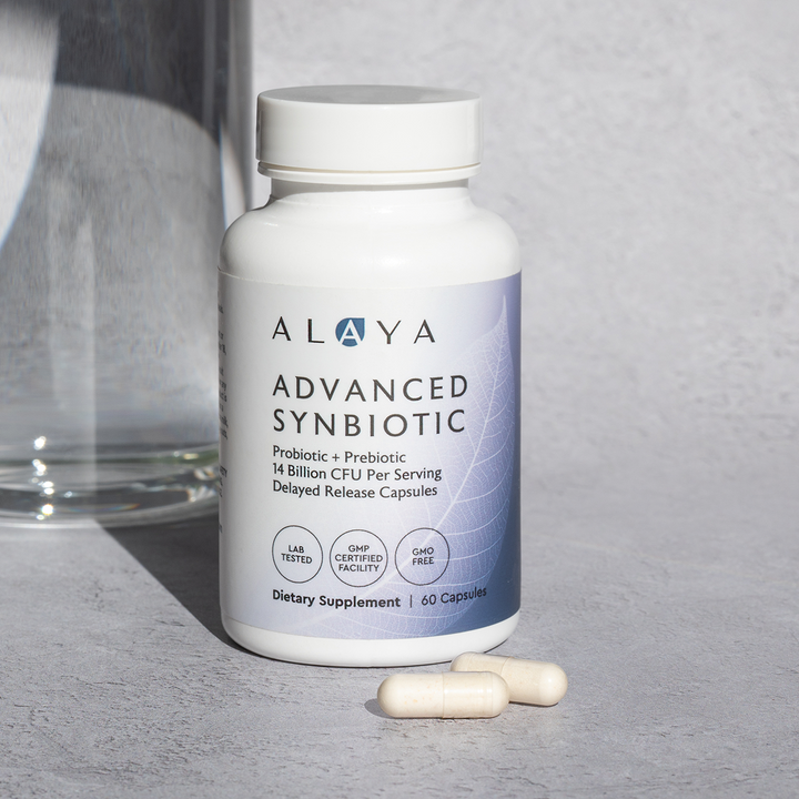 Alaya Advanced Synbiotic supplement bottle on a gray surface with two capsules beside it.